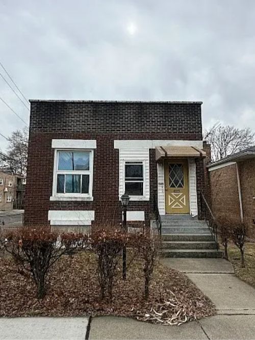 Brick bungalow with white trim, two windows, and a yellow front door with a diamond window, reached by concrete steps.